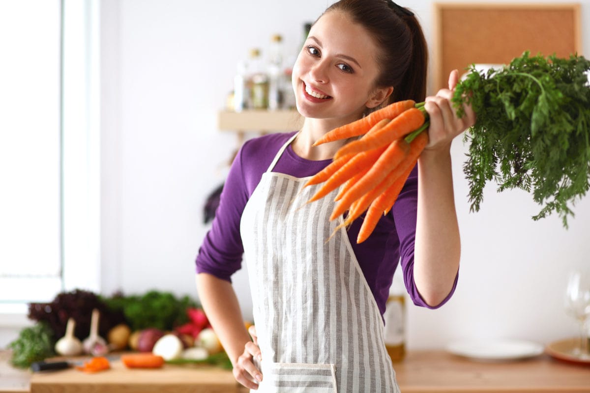 happy young woman holding a carrot bunch in kitchen
