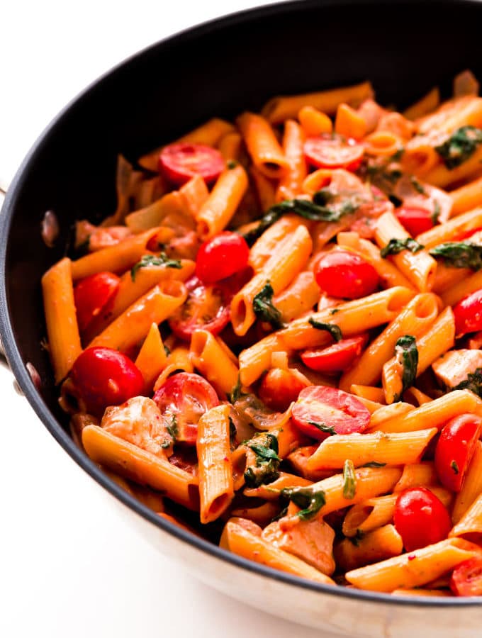 Red pesto penne pasta with chicken, spinach, baby tomatoes and onions in a large skillet.