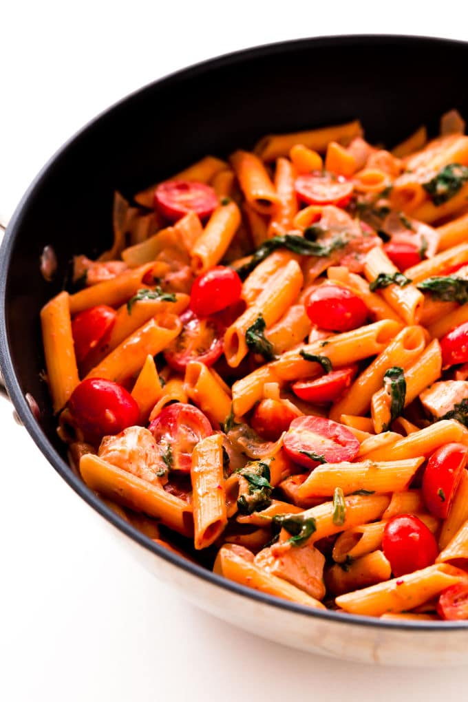 Red pesto penne pasta with chicken, spinach, baby tomatoes and onions in a large skillet.