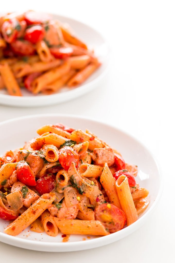 Red pesto penne pasta with chicken served in white plates.