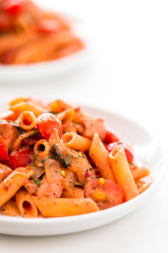 Red pesto penne pasta with chicken served in white plates.
