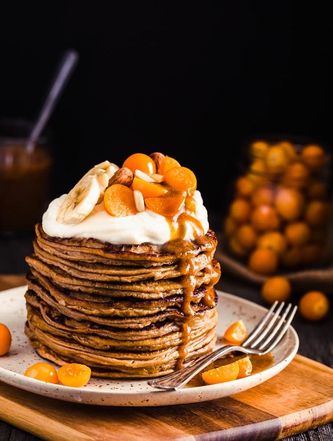 A stack of pancakes with whipped cream and fruits on top.