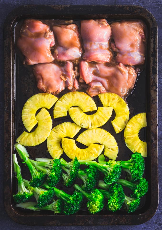 Chicken thighs, pineapple slices and broccoli florets on a baking pan.
