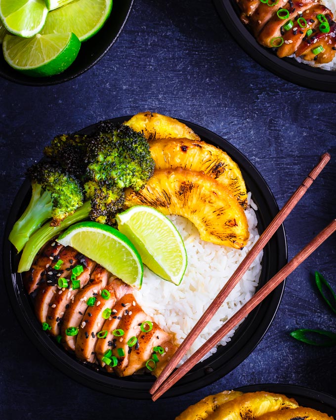 A bowl containing rice, teriyaki chicken, pineapple slices and broccoli florets.